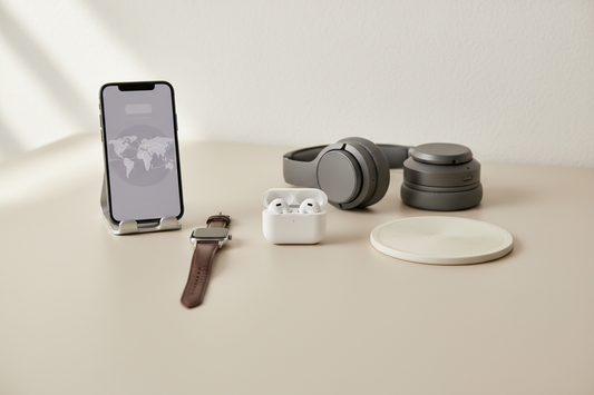 Essential tech accessories for digital nomads including wireless earbuds, smartphone charging stand, smartwatch with premium band, and wireless charging pad on minimalist desk
